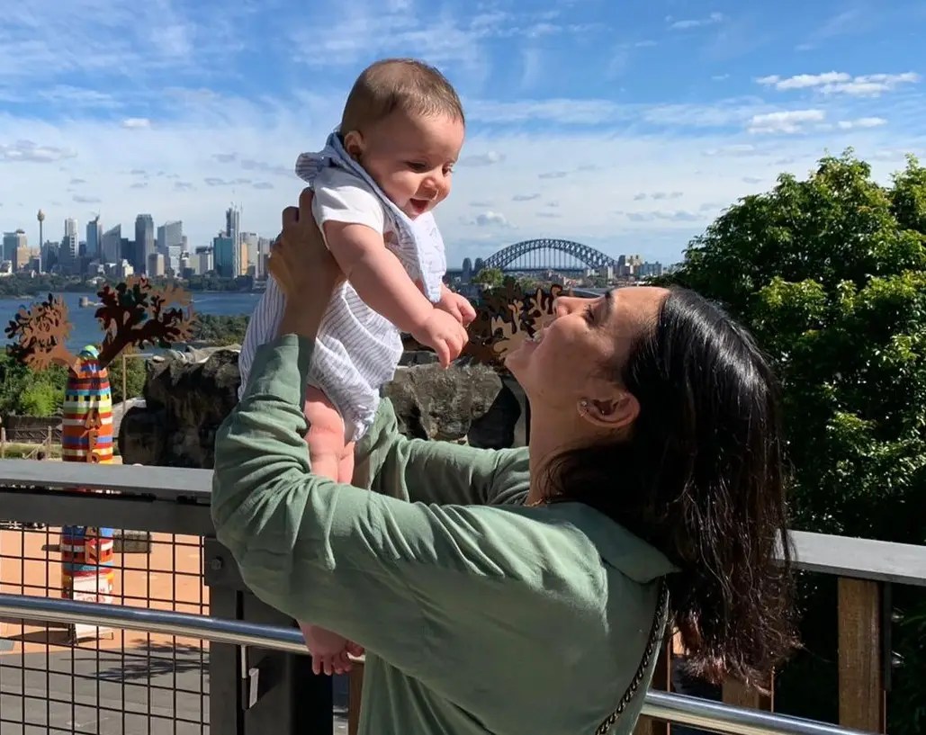 Nesli Avgan, founder of SaluStory, holding her son up against the Sydney skyline.