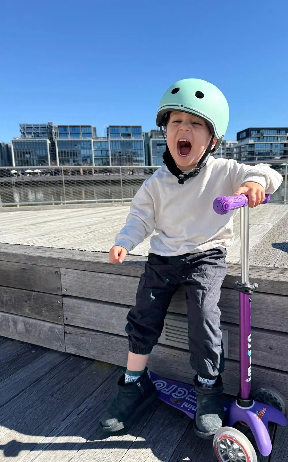 Nesli&rsquo;s son on his scooter, mid-laugh, in a bike helmet.